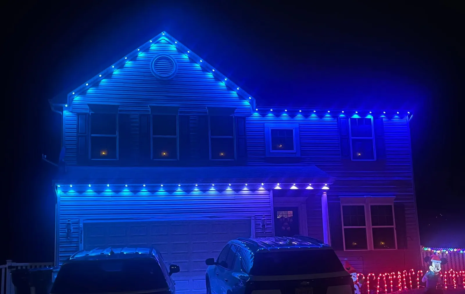 Two-story home with blue permanent lighting across the gables and garage line