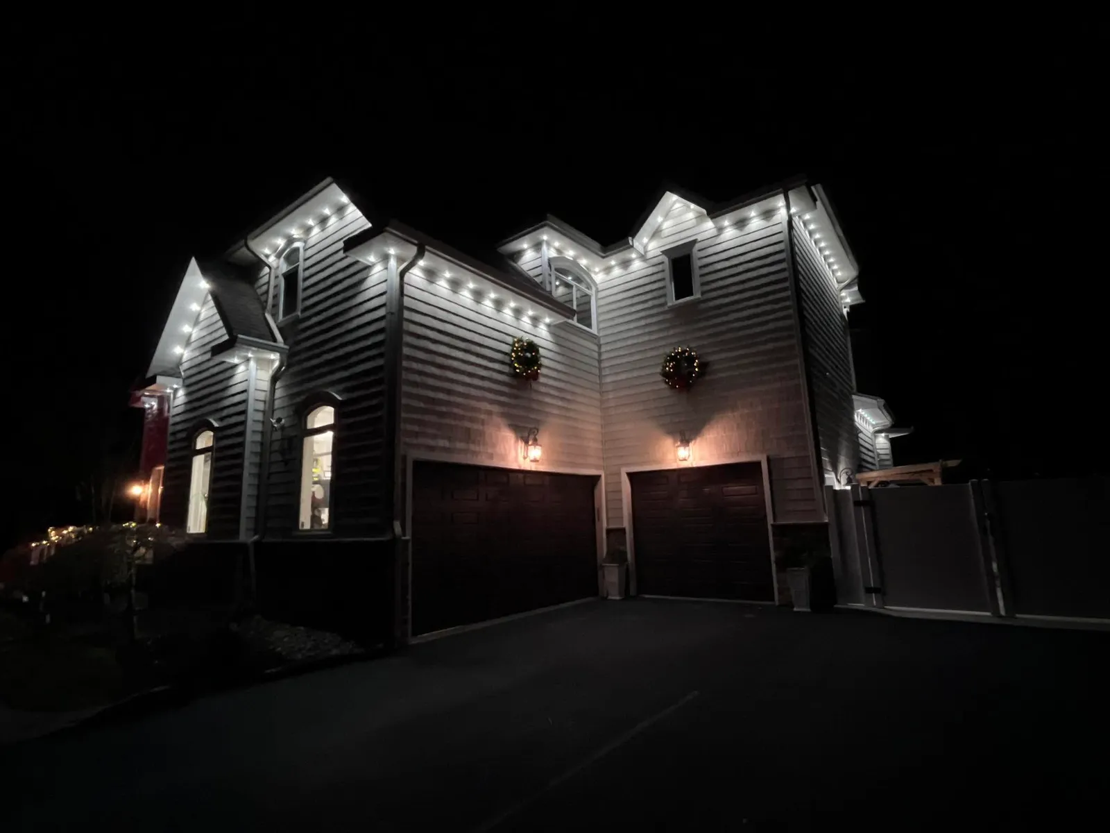 Stone-front home with cool white permanent lighting on every dormer and gable