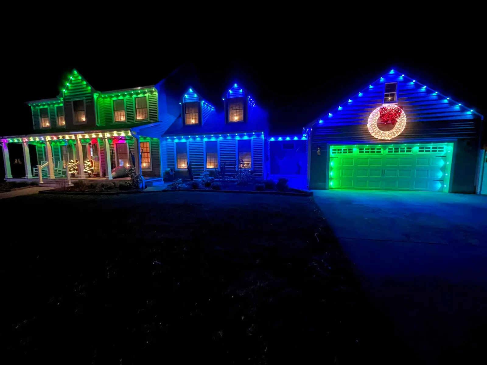 Home with green and blue permanent lighting scenes and a lit wreath over the garage