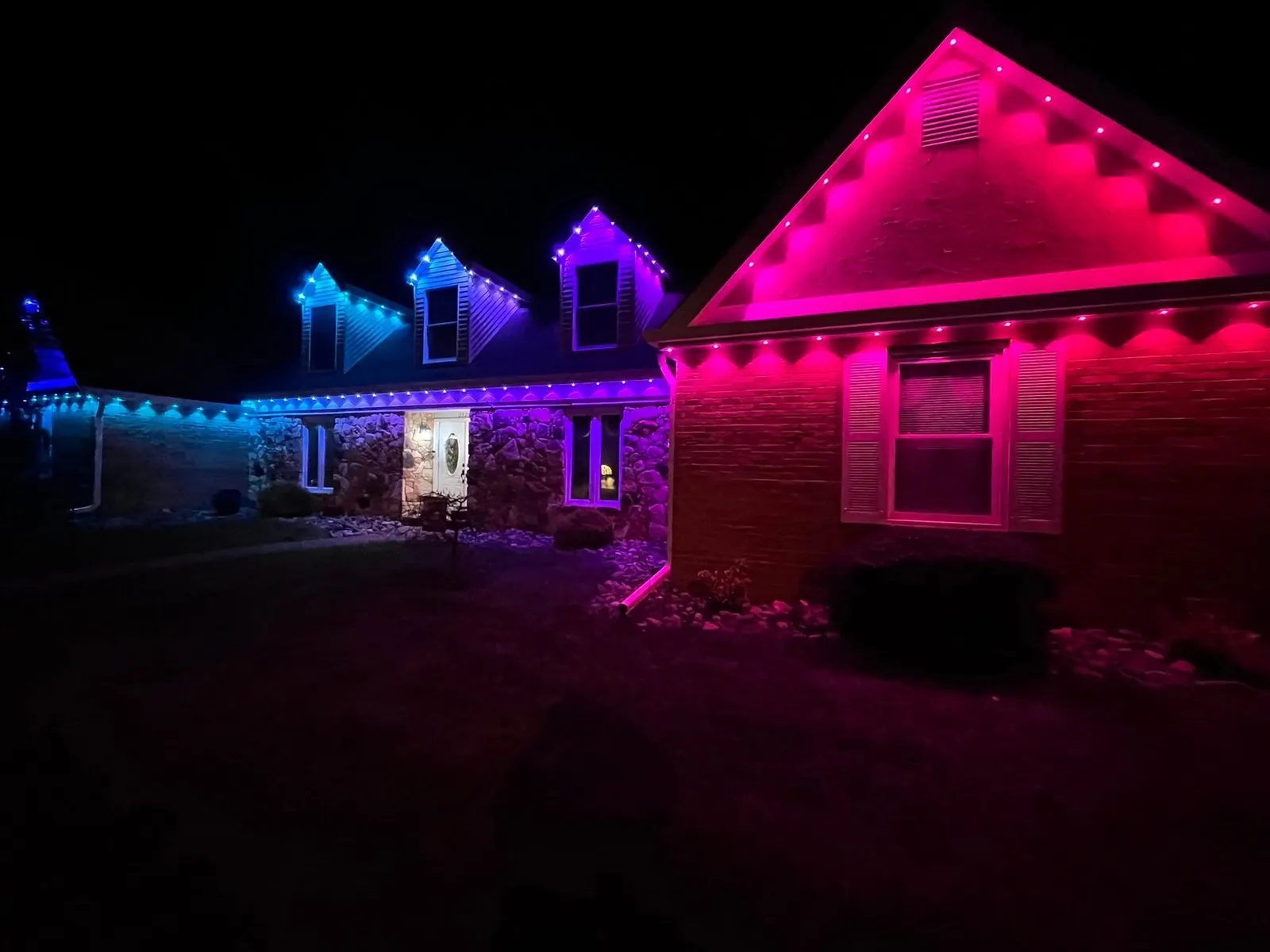 Home with pink, blue, and red permanent lighting zones across dormers at night