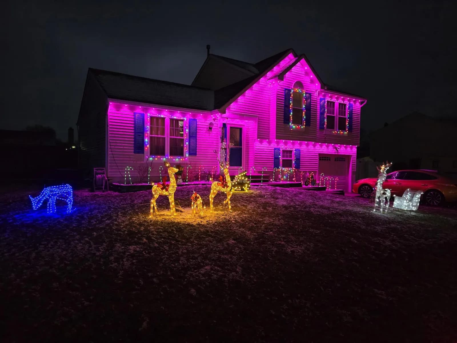 Split-level home washed in pink permanent lighting with holiday yard decorations