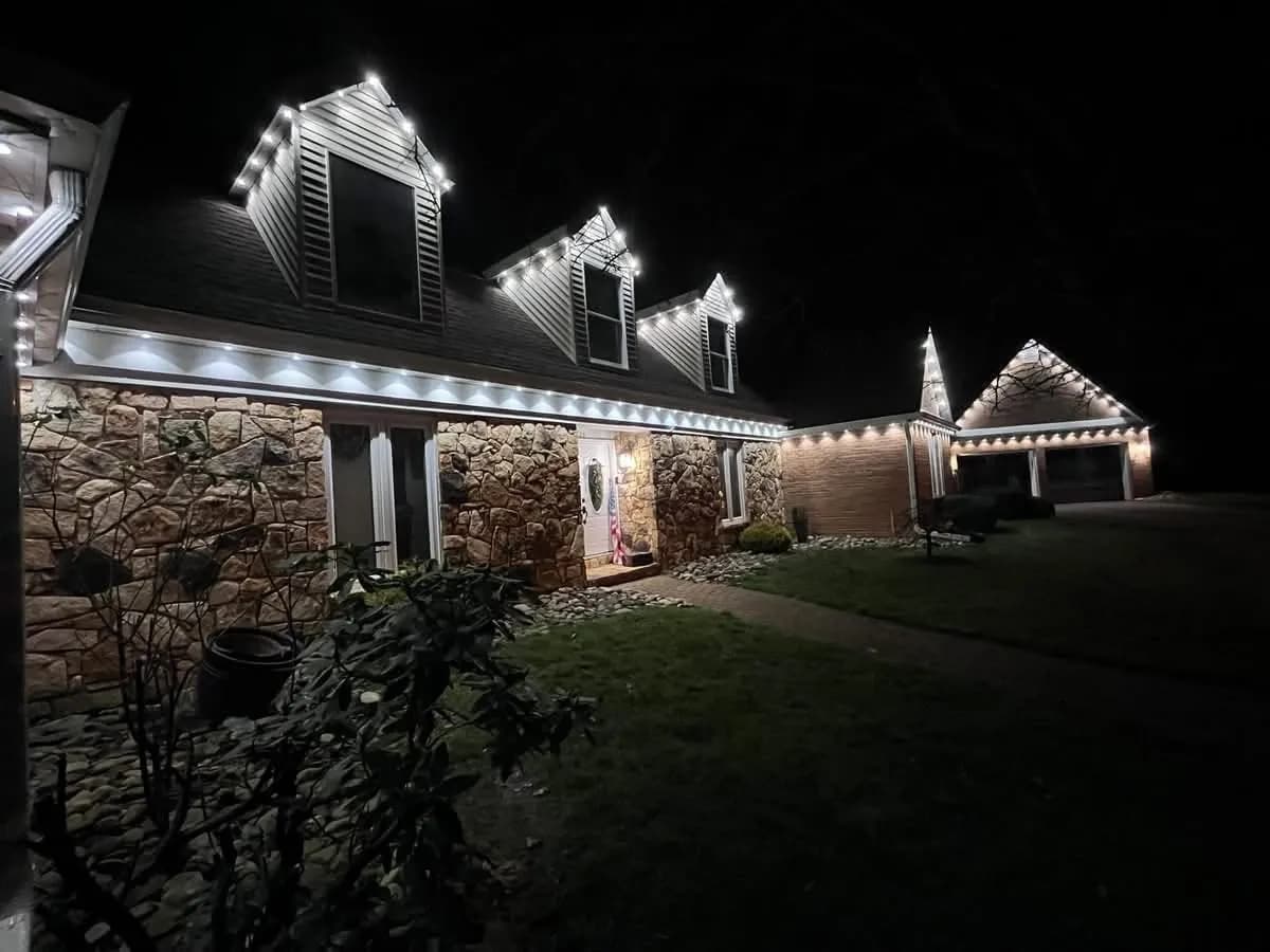 Warm white Govee permanent lighting outlining the rooflines of a stone-front ranch home at night